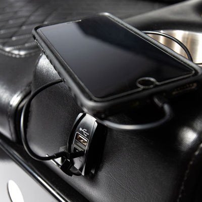 An iPhone being charged in the built-in USB ports on a black Comfort Before Pain Waiting Room Bench by TATSoul. 