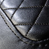 A close-up view of the diamond cushion stitching on the black vinyl seat of the Comfort Before Pain Waiting Room Bench by TATSoul.  