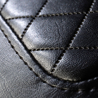 A close-up view of the diamond cushion stitching on the black vinyl seat of the Comfort Before Pain Waiting Room Bench by TATSoul.  
